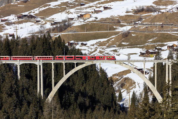 Red train of Rhaetian Railway on Langwies Viaduct surrounded by woods Canton of Graubünden Switzerland Europe