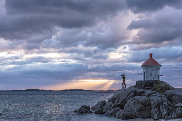 Photographer in action on cliffs while the midnight sun lights up the blue sea Eggum Vestvagøy Lofoten Islands Norway Europe