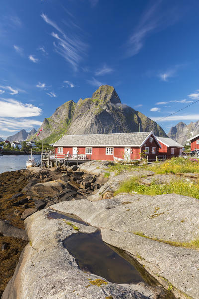 Typical houses of fishermen called Rorbu framed by rocky peaks and blue sea Reine Moskenes Lofoten Islands Norway Europe
