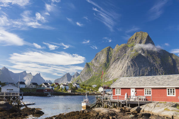 Typical house of fishermen called Rorbu framed by rocky peaks and blue sea Reine Moskenes Lofoten Islands Norway Europe