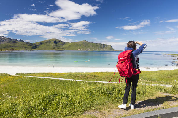 Photographer in action in the green meadows surrounded by turquoise sea and fine sand Ramberg Lofoten Islands Norway Europe