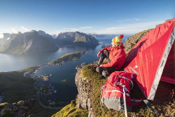 Hiker admires the blue sea framing the village from a tent on top of peak Reinebringen Moskenes Lofoten Islands Norway Europe