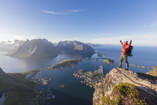 Hiker admires the blue sea and typical village from the high rocky summit  Reinebringen Moskenes Lofoten Norway Europe