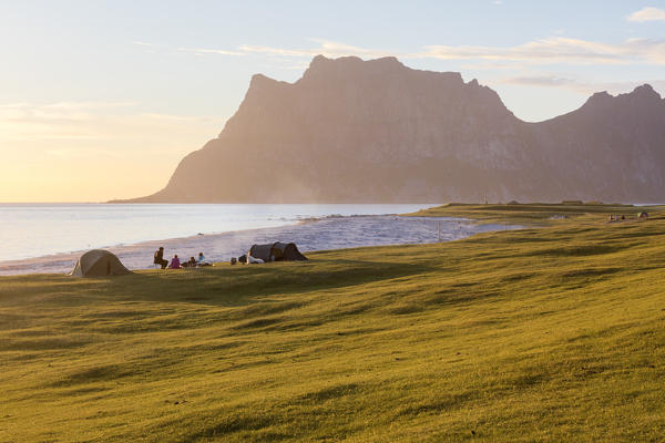 Camping tents on green meadows next to sea lighted up by midnight sun Uttakleiv Lofoten Islands Northern Norway Europe