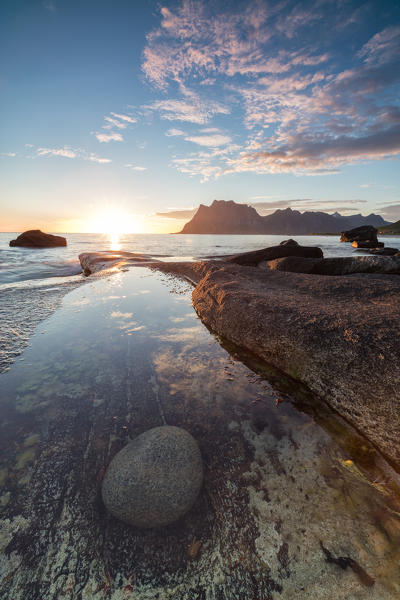 Pink clouds and midnight sun are reflected in the blue sea framed by rocky peaks Uttakleiv Lofoten Islands Norway Europe