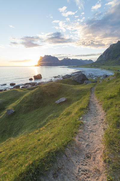 The midnight sun lights up the green meadows and path leading to the blue sea Uttakleiv Lofoten Islands Norway Europe