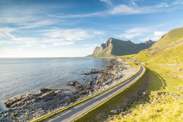 The night sun shines on the asphalt road between sea and rocky mountains Vikten Nord Trøndelag Lofoten Islands Norway Europe