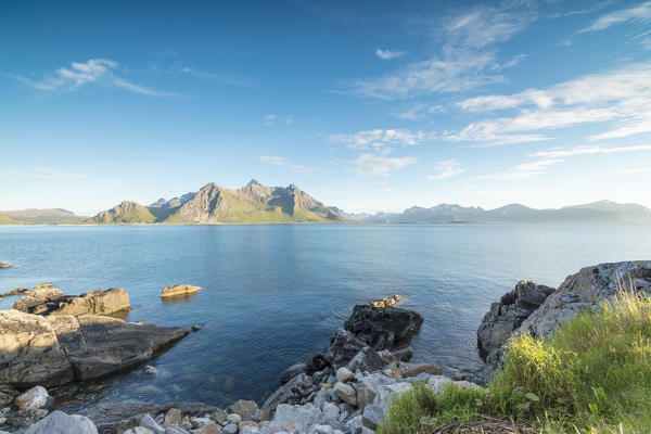 Sun shines on the blue sea and the rocky peaks at night during summer Vikten Nord Trøndelag Lofoten Islands Norway Europe