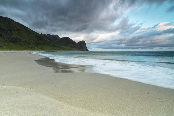 Pink clouds of midnight sun reflected on the blue sea and sandy beach Unstad Vestvagøy Lofoten Islands Norway Europe