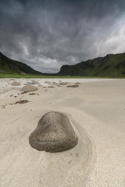 Rock on sandy beach frames the dark clouds over the peaks Unstad Vestvagøy Lofoten Islands Norway Europe
