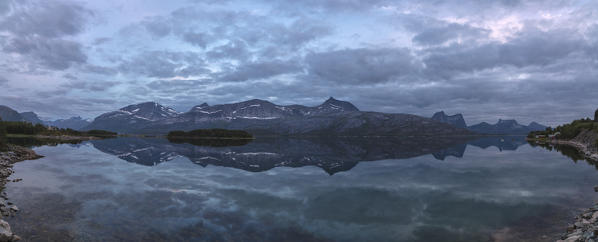 Blue sky and clouds at dusk lights up the rocky peaks reflected in the clear sea Vidrek Ofotfjorden Norway Europe