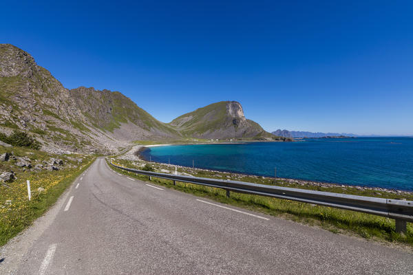 Asphalt road between the blue sea and the rocky mountains Vaeroy Island Nordland county Lofoten archipelago Norway Europe