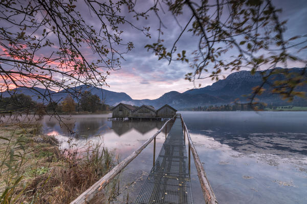 Purple sky at sunset and wooden huts are reflected in the clear water of Kochelsee Schlehdorf Bavaria Germany Europe