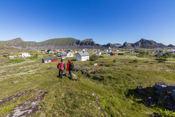 Hikers admire the village of Sorland surrounded by green meadows Vaeroy Island Nordland county Lofoten archipelago Norway Europe