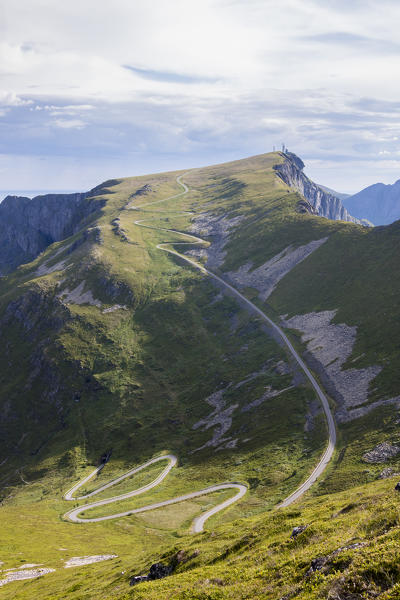 Steep road of curves on green meadows framed by rocky peaks Sorland Vaeroy Island county of Nordland Lofoten Norway Europe