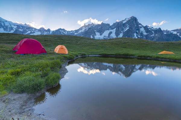 Camping tents in the green meadows surrounded by alpine lake at dusk Mont De La Saxe Courmayeur Aosta Valley Italy Europe