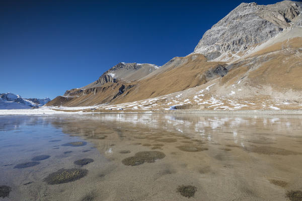 The blue sky frames the rocky peaks reflected in the alpine lake Julier Pass canton of Graubünden Engadine Switzerland Europe