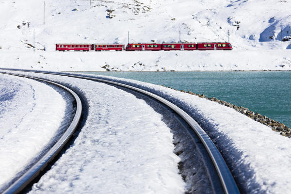 Bernina Express train in the snowy valley surrounded by Lake Bianco Bernina Pass Canton of Graubünden Engadin Switzerland Europe