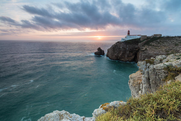 Pink sky at sunset frames the lighthouse overlooking the Atlantic Ocean Cabo De Sao Vicente Sagres Algarve Portugal Europe