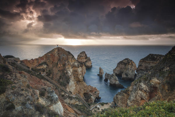 Hiker on top of cliffs surrounded by the ocean under the cloudy sky at sunrise Ponta Da Piedade Lagos Algarve Portugal Europe