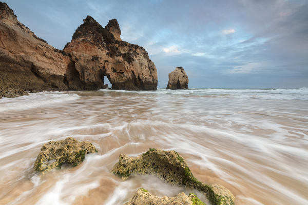 Clouds frame the rough sea and cliffs at sunset Praia Dos Tres Irmaos Portimao Algarve Portugal Europe