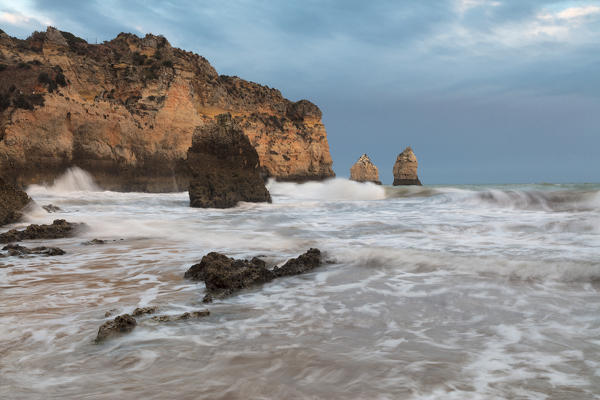 Clouds frame the rough sea and cliffs at sunset Praia Dos Tres Irmaos Portimao Algarve Portugal Europe