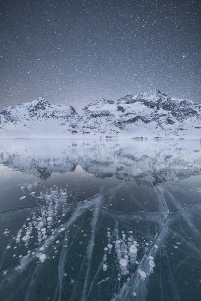 The icy surface of Lago Bianco frames snowy peaks and starry sky Bernina Pass canton of  Graubünden Engadine Switzerland Europe