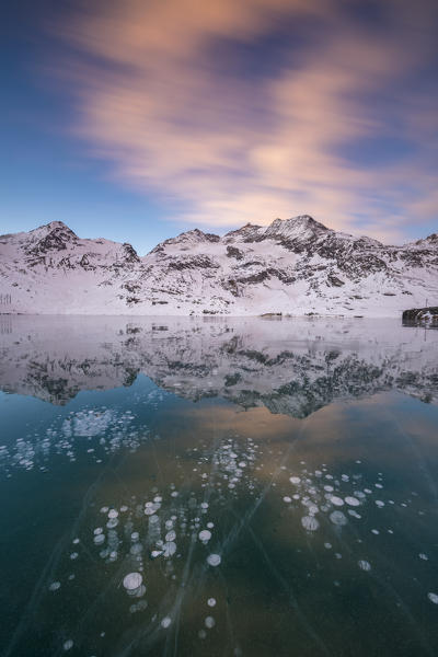 Ice bubbles and pink clouds frame the frozen Lago Bianco at dawn Bernina Pass canton of  Graubünden Engadine Switzerland Europe
