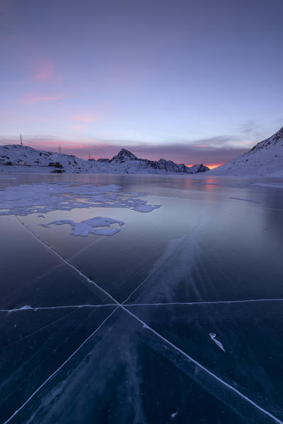 The frozen Lago Bianco framed by the first lights of dawn Bernina Pass canton of Graubünden Engadine Switzerland Europe