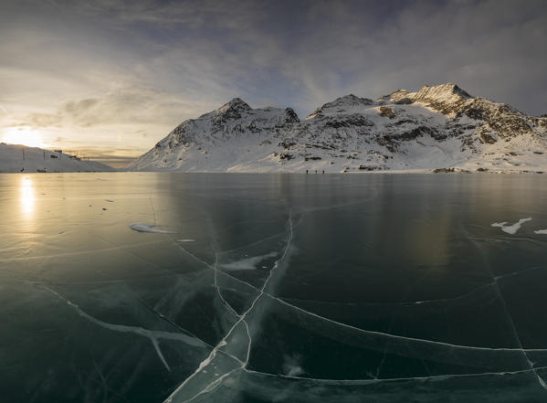 The frozen surface of Lago Bianco framed by snowy peaks at dawn Bernina Pass canton of Graubünden Engadine Switzerland Europe