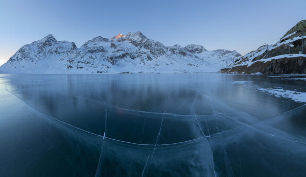 Panorama of frozen Lago Bianco surrounded by snowy peaks at dusk Bernina Pass canton of Graubünden Engadine Switzerland Europe