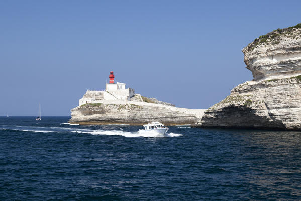 Boat in the crystal blue sea surrounded by granite white cliffs and lighthouse Lavezzi Islands Bonifacio Corsica France Europe