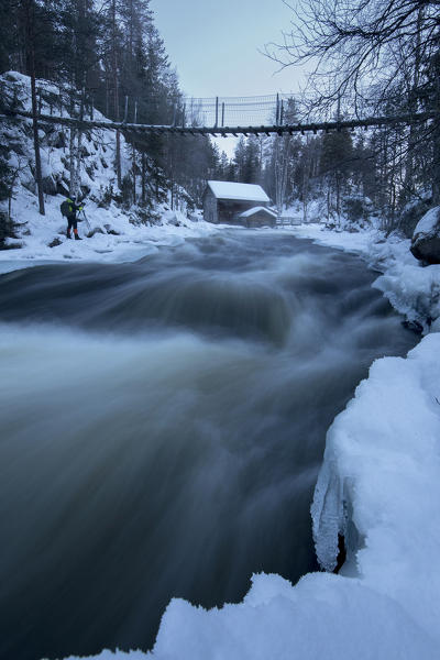 A wooden hut surrounded by the river rapids and snowy woods at dusk Juuma Myllykoski Lapland region Finland Europe