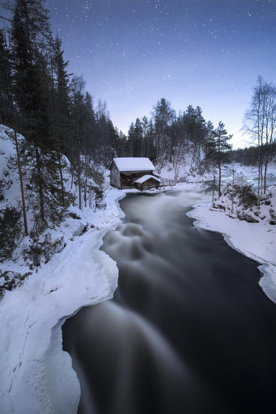 Starry sky on wooden hut surrounded by the river rapids and snowy woods Juuma Myllykoski Lapland region Finland Europe