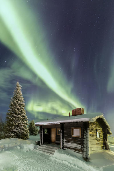 The Northern Lights frames the wooden hut in the snowy woods Pallas Yllästunturi National Park Lapland region Finland Europe