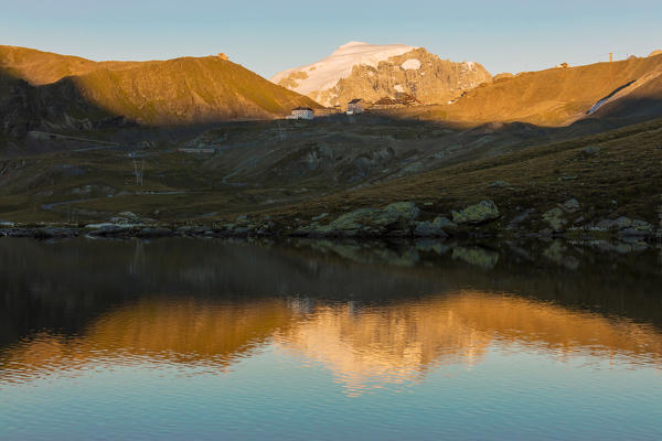 The rocky peaks are reflected in the alpine lake at sunset Stelvio Pass Valtellina Lombardy Italy Europe