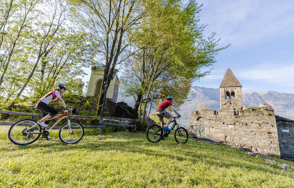 Cyclists on mountain bike around the Abbey of San Pietro in Vallate Piagno Sondrio province Valtellina Lombardy Italy Europe