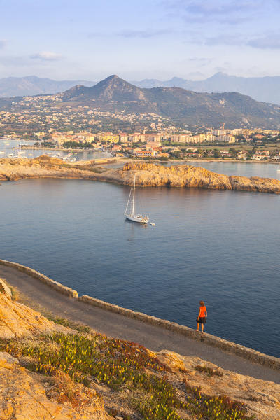 Tourist on a road admires the sail boat in the clear sea around the village of Ile Rousse Balagne Region Corsica France Europe