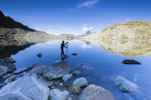 Photographer in action on rocks in the clear water of Lago Nero at sunrise Chiavenna Valley Valtellina Lombardy Italy Europe