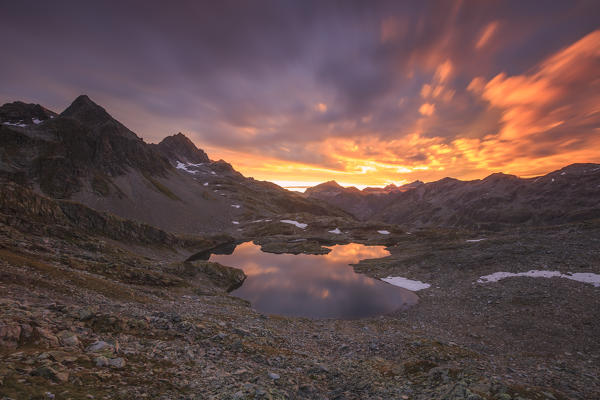 Fiery sky at dawn reflected in Lai Ghiacciato framed by peaks Val Ursaregls Chiavenna Valley Valtellina Lombardy Italy Europe