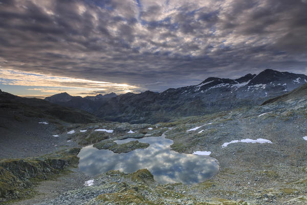 Clouds at dawn are reflected in Lai Ghiacciato framed by peaks Val Ursaregls Chiavenna Valley Valtellina Lombardy Italy Europe