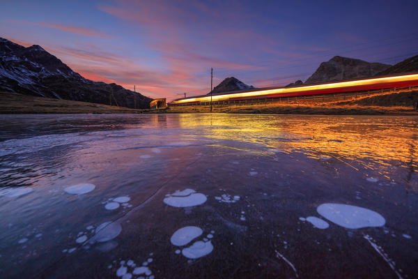 Bernina Express train next to the frozen Lake Pitschen at sunset Bernina Pass Canton of Graubünden Engadine Switzerland Europe