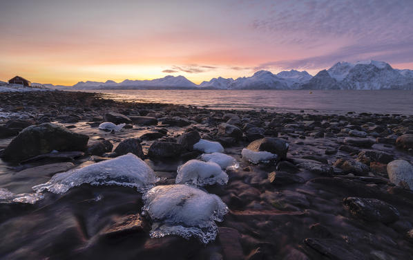 Fiery sky at sunset on snowy peaks and frozen sea framed by rocks covered with ice Djupvik  Lyngen Alps Tromsø Norway Europe