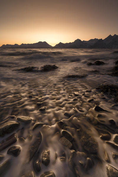 Fiery sky at sunset on the waves of cold sea crashing on the rocks Djupvik Lyngen Alps Tromsø Norway Europe