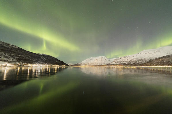 The Northern Lights is reflected in the icy sea surrounded by snowy peaks Manndalen Kafjord Lyngen Alps Tromsø Norway Europe