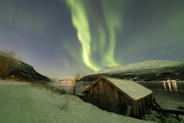 The Northern Lights reflected in the icy sea frames a typical Rorbu Manndalen Kafjord Lyngen Alps Tromsø Norway Europe