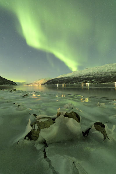 Northern Lights reflected in the cold sea frames the rocks covered with ice Manndalen Kafjord Lyngen Alps Tromsø Norway Europe