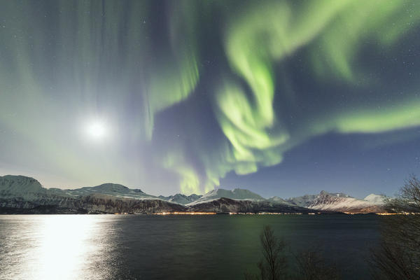 The Northern Lights and moon are reflected in the cold sea in the polar night Manndalen Kafjord Lyngen Alps Tromsø Norway Europe