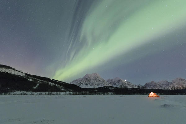 A tent in the snow lighted up by Northern Lights and starry sky in the polar night Svensby Lyngen Alps Tromsø Norway Europe