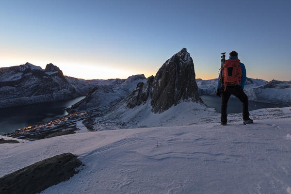 Hiker admires Mount Segla from peak Hesten with the village of Fjordgard on left  and Mefjorden on the right Senja Norway Europe